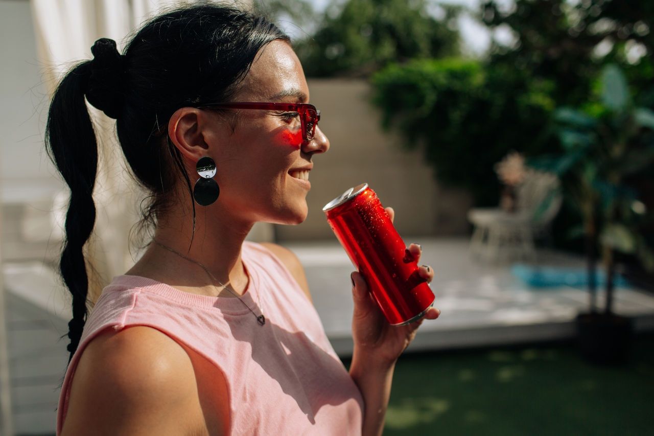A girl on an orange background with a red tin can in her hands. Cheerful girl, advertising shooting. High quality photo. High quality photo