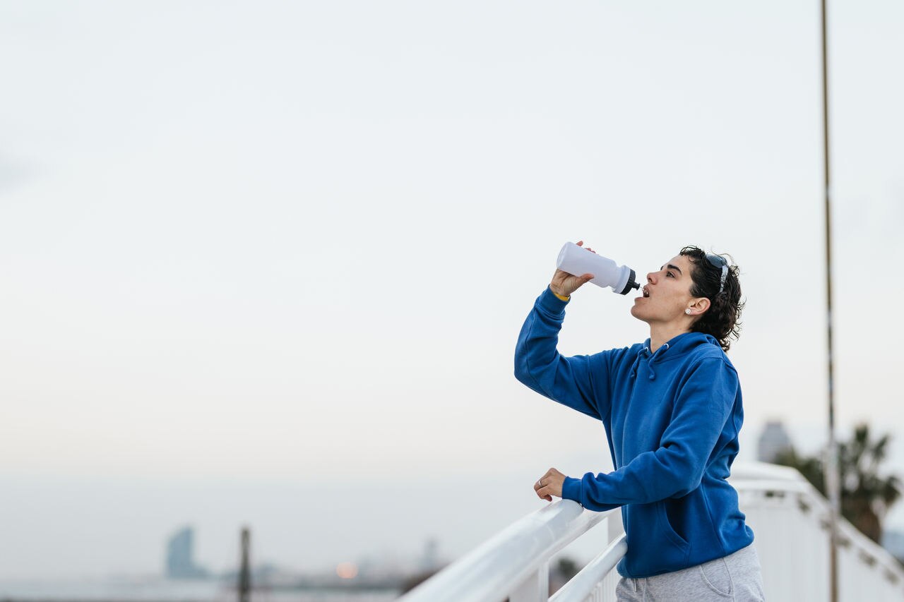 Athletic woman drinking water from a bottle after intense physical activity, exercising in the city to stay healthy.