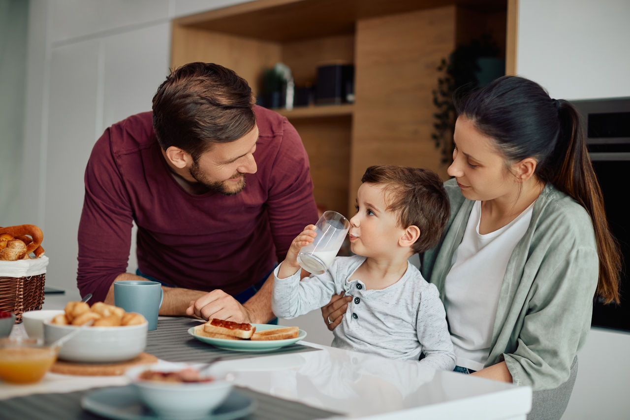 Small boy drinking milk while having breakfast with his parents at dining table at home.
