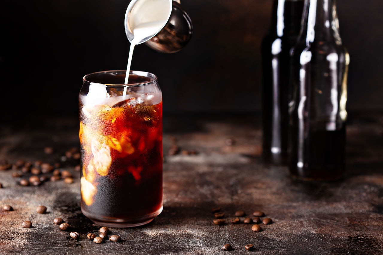 Cold brew iced coffee in a glass with milk or creamer pouring over