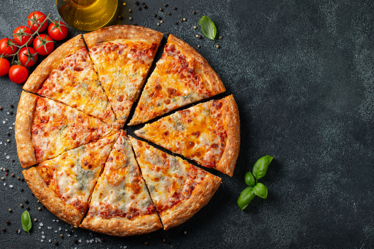 Delicious Italian pizza four cheeses with Basil, tomatoes and olive oil on a dark concrete table. Top view with copy space. Flat lay