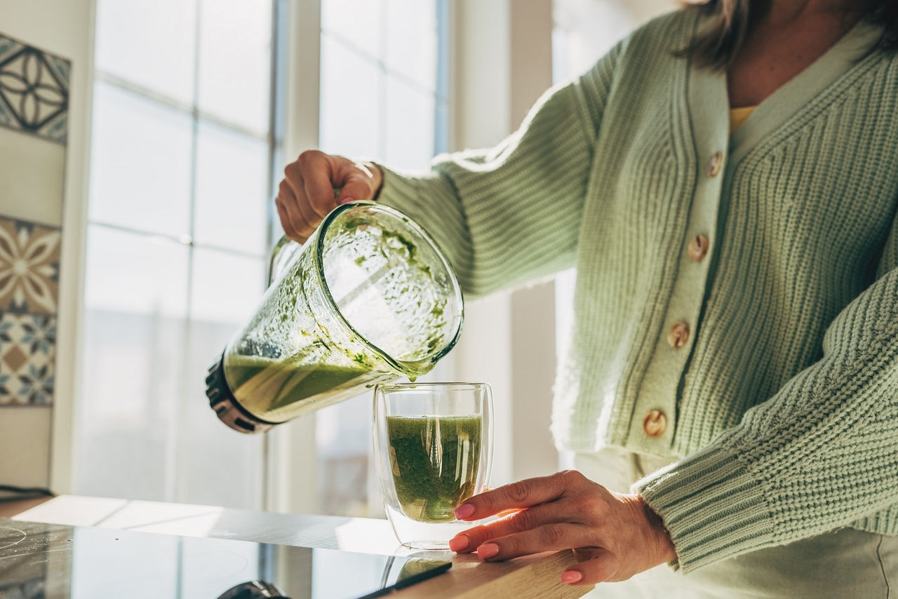 Young Woman Making Detox Smoothie At Home. Woman pouring smoothie to glass. healthy food concept