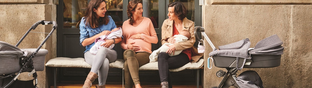 Expectant sitting amidst friends carrying babies outside restaurant