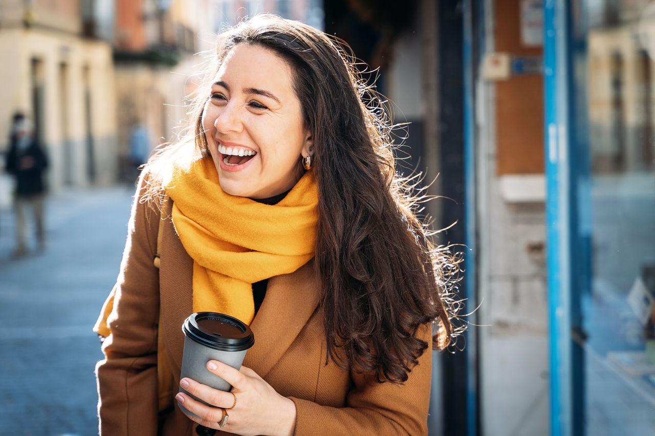 Horizontal mid waist view of beautiful brunette woman drinking coffee walking in the street in autumn. People lifestyles
