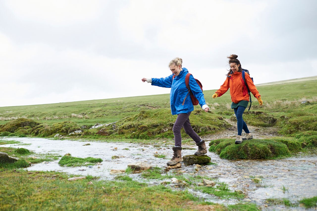 Hikers carefully step on rocks to cross a small stream