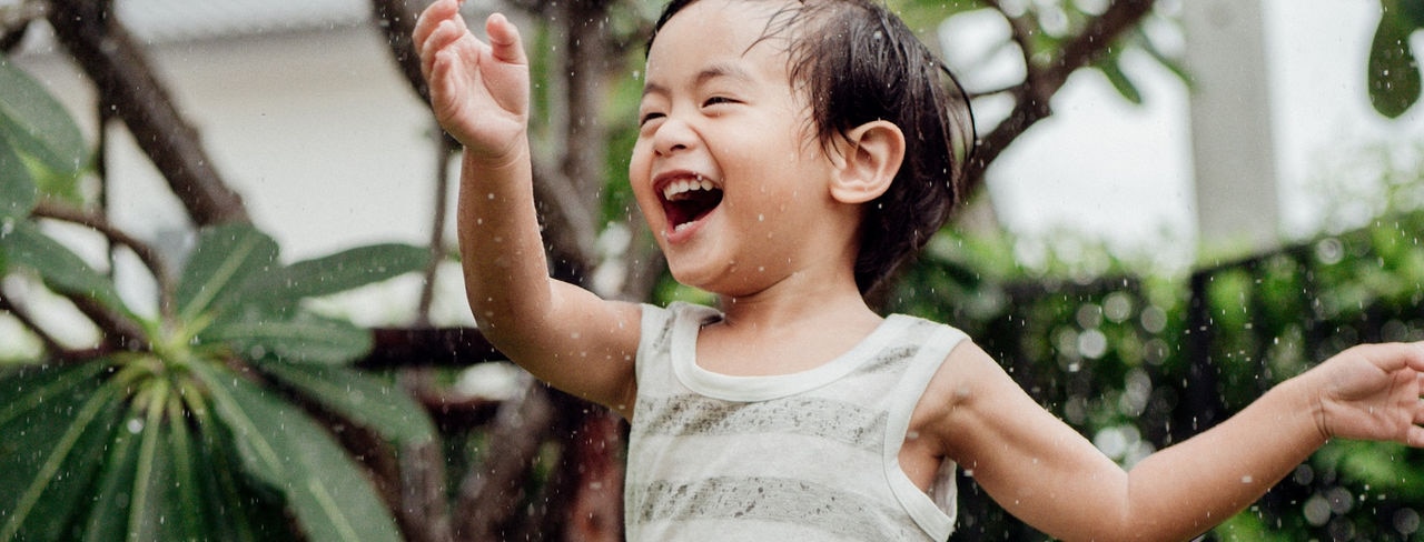 Happy baby boy plays with Sprinkler in garden.