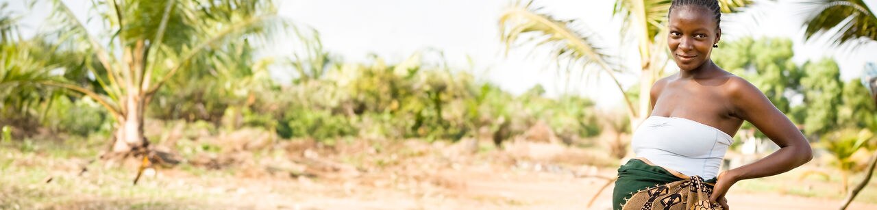A pregnant African woman with her hands on her back smiling into the distance.