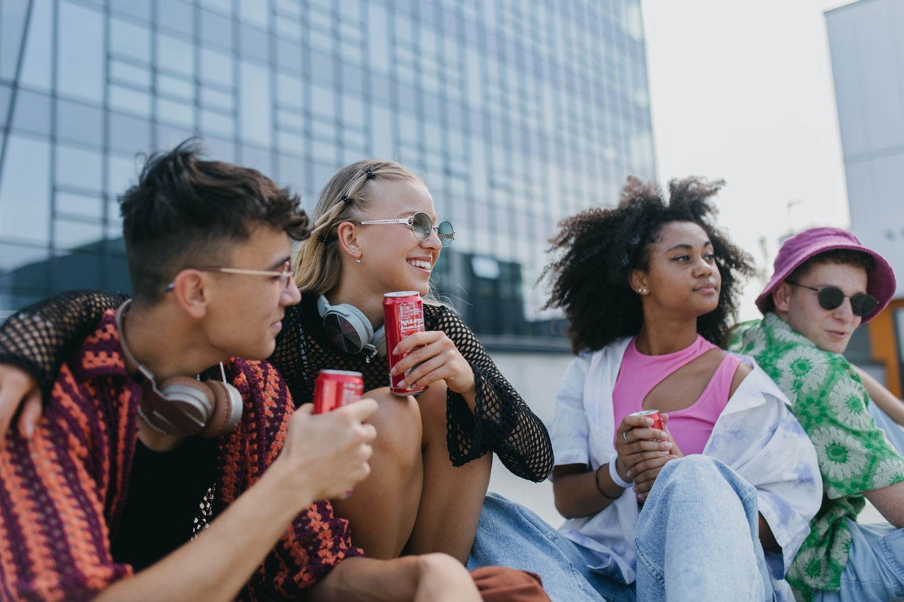 Diverse group of generation z friends hanging out together, drinking soda from cans outdoors in the city. Young stylish zoomers drinking energy drinks from cans to refresh themselves. Students spending time during summer break. Concept of recycling of aluminium cans and sustainable drink containers.