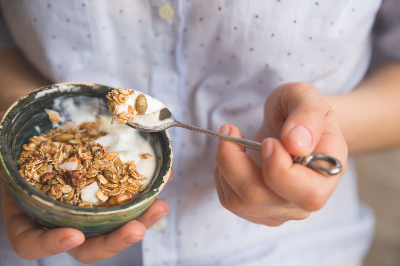 Young woman with muesli bowl. Girl eating breakfast cereals with nuts, pumpkin seeds, oats and yogurt in bowl. Girl holding homemade granola. Healthy snack or breakfast in the morning.