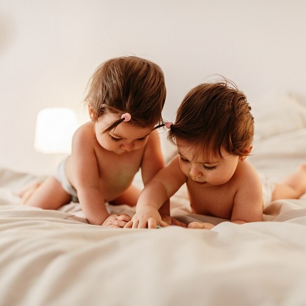Two baby girls lying on the bed , looking at a mobile phone
