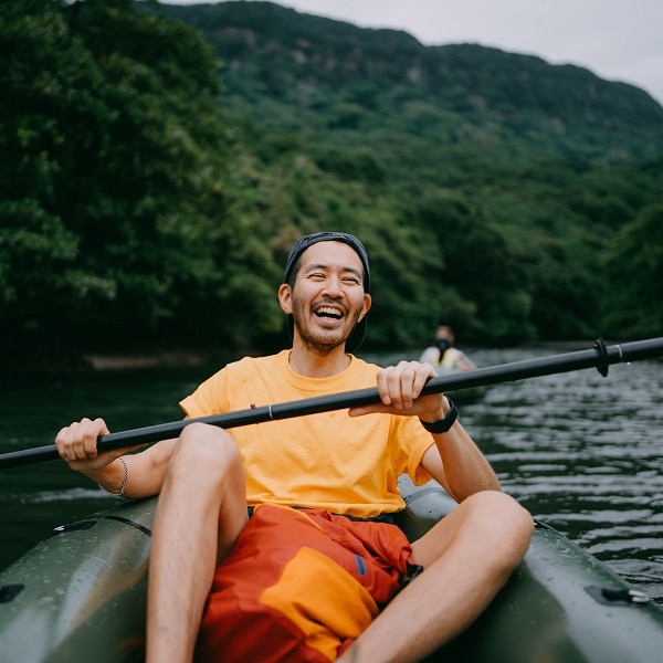 Japanese man paddling packraft in mangrove river and laughing, Iriomote-Ishigaki National Park of the Yaeyama Islands, Okinawa, Japan