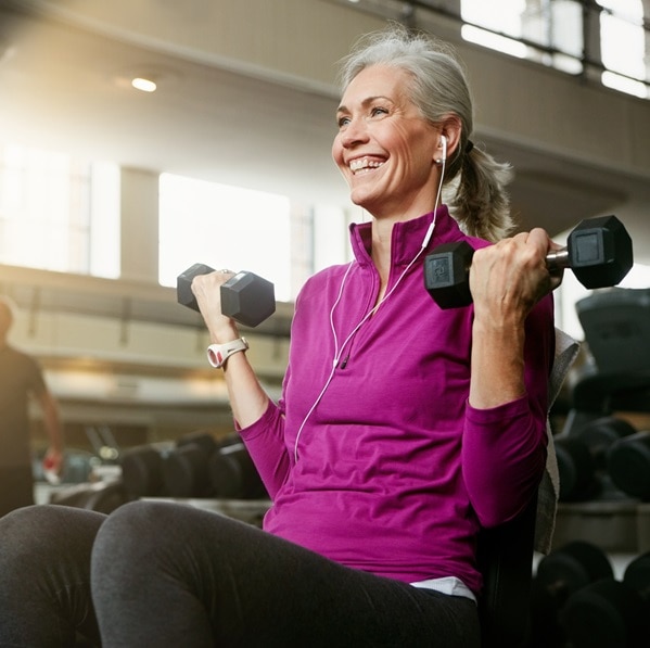 Portrait of a happy senior woman working out with weights at the gym