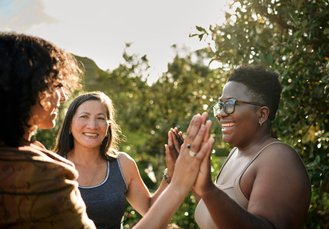 Laughing woman and a group of other women standing with her hands together during an exercise at a wellness retreat in summer