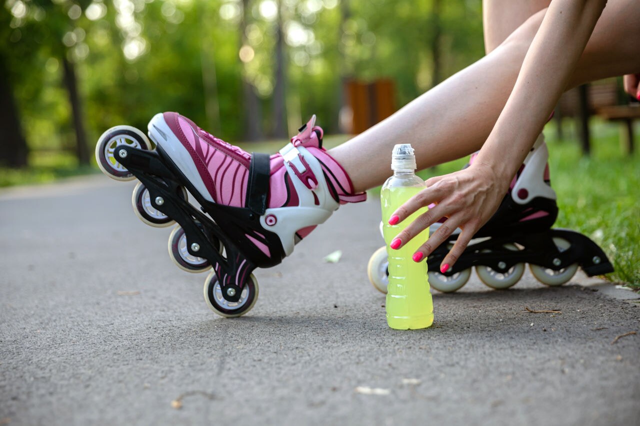 A girl sitting on a bench reaches for a bottle of drink.