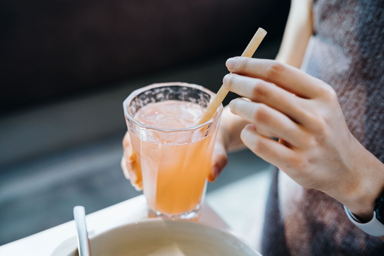 Close up shot of young woman drinking a glass of fresh iced pink lemonade with eco-friendly straws during meal in cafe. Sustainable lifestyle, eco trend, going green lifestyle