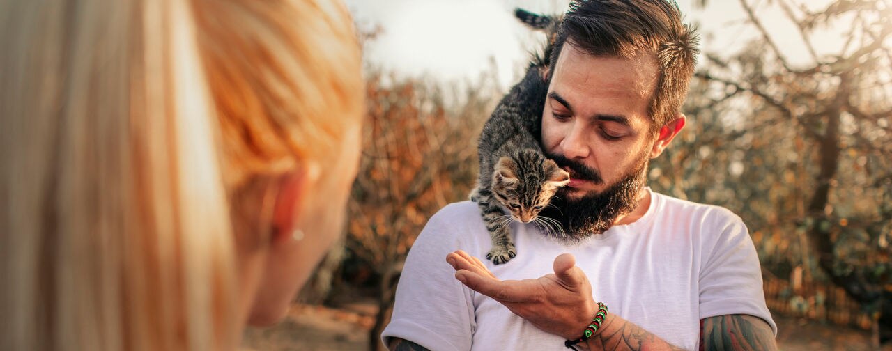 Tattooed Couple On Farm Together. Man carrying cute kitten on his shoulder.