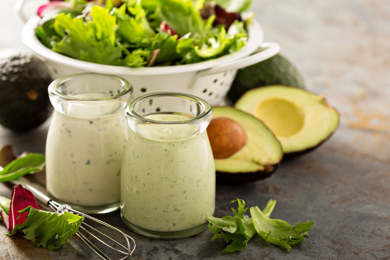 Avocado ranch dressing in small jar with salad leaves in a colander.