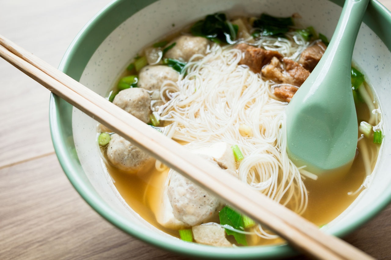 Rice vermicelli noodle and meatball Braised pork and tofu pork in the bowl have chopstick and spoon on the wood table 