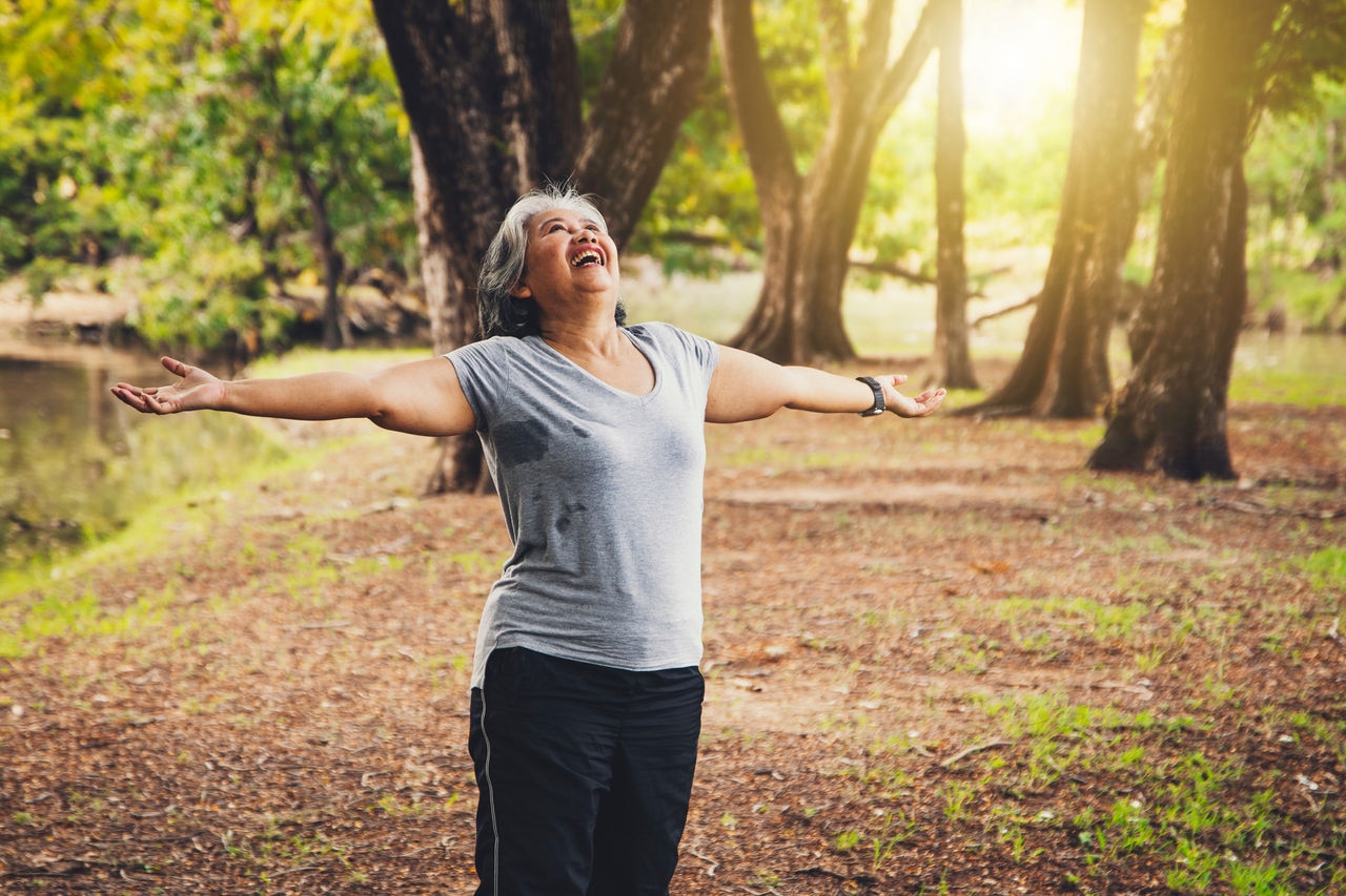 Healthy and strong happiness of a senior woman : Senior woman with a cheerful heart, standing in the liberty of fresh air in a garden with trees and fresh nature.