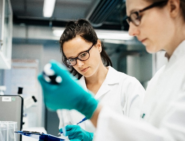 Two scientists working together in the lab, concentrating while using a mechanical pipette.