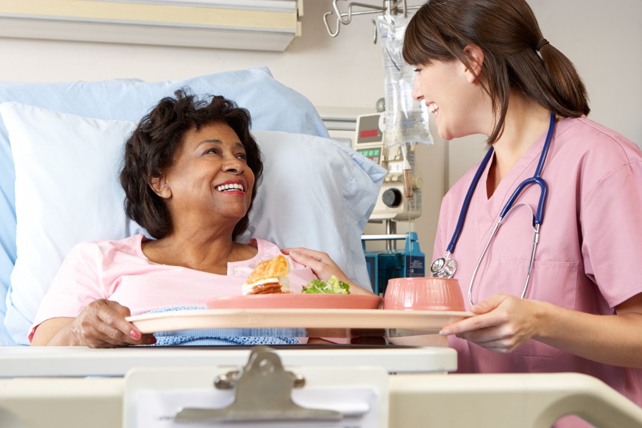 Female Nurse Serving Senior Female Patient Meal In Hospital Bed
