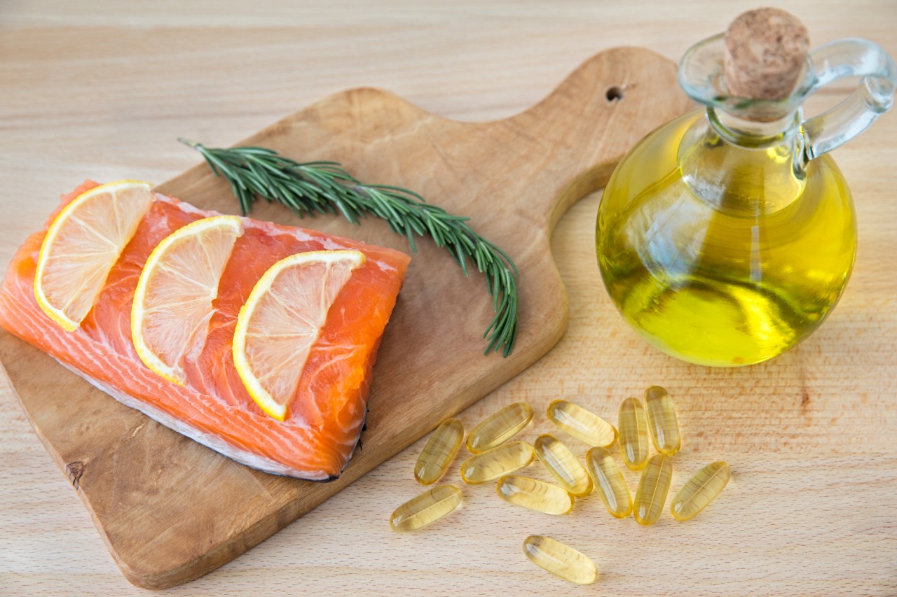 Fish oil capsules, cod liver, and salmon fillet on wooden surface
