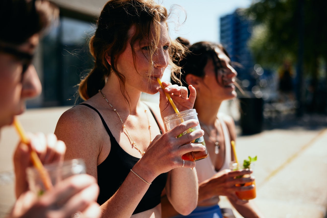 Group of young female friends in sportswear sitting outside after a yoga class drinking freshly made fruit drinks