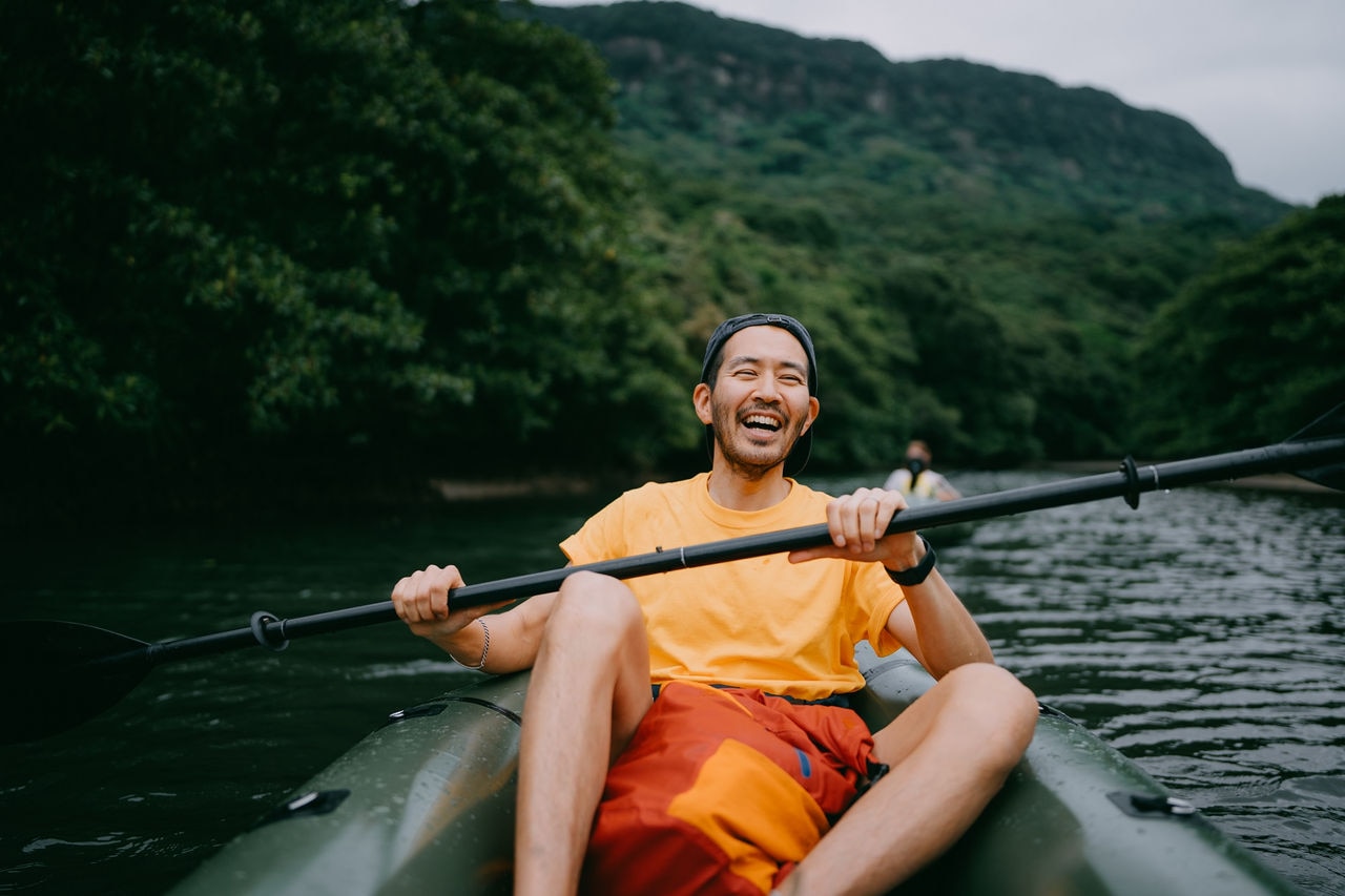 Japanese man paddling packraft in mangrove river and laughing, Iriomote-Ishigaki National Park of the Yaeyama Islands, Okinawa, Japan