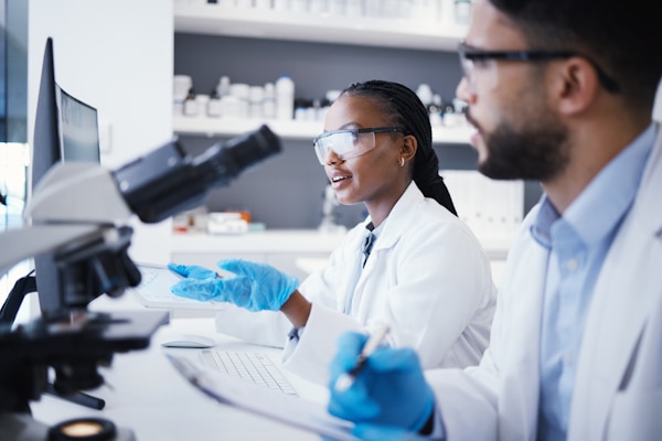 Scientist man, woman and checklist in laboratory with microscope, pc or analysis for virus dna at pharma job. Teamwork, medical research and digital touchscreen for data, info and study for wellness