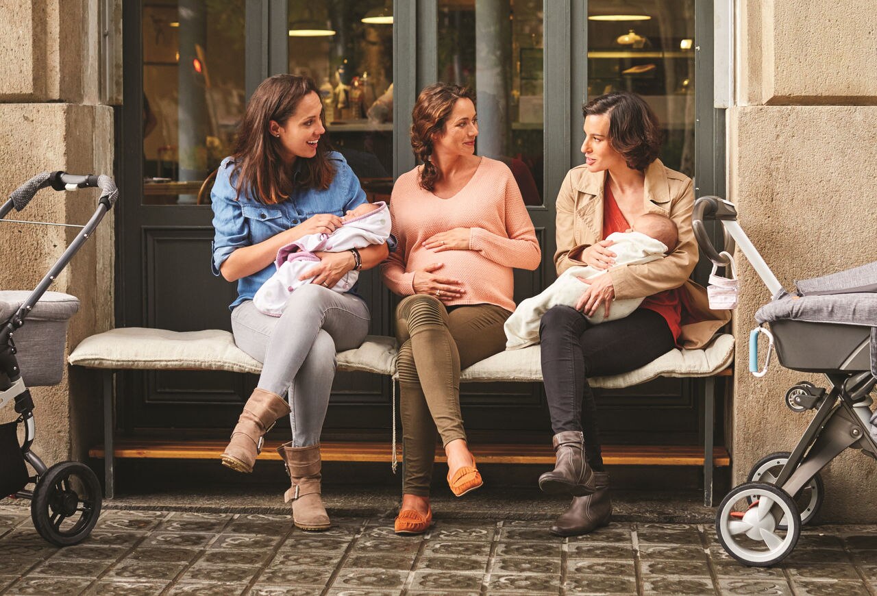 Expectant sitting amidst friends carrying babies outside restaurant