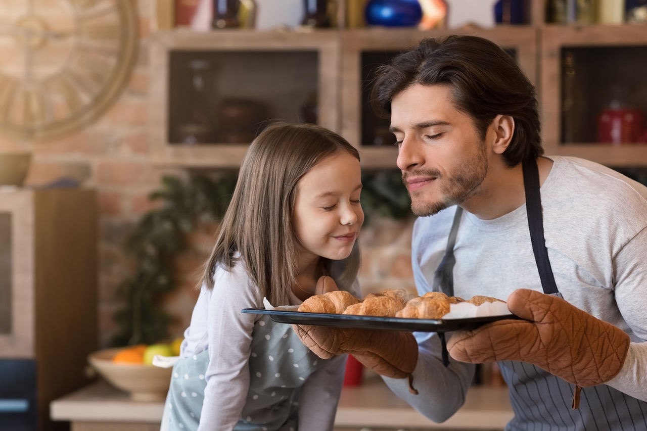 Homemade pastries. Cute little girl and her dad holding tray and smelling freshly baked croissants, enjoying result of their cooking