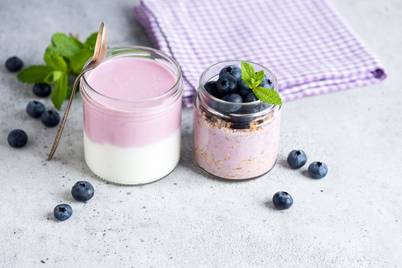Purple greek yogurt with blueberries in a jar, grey concrete background, closeup view with copy space