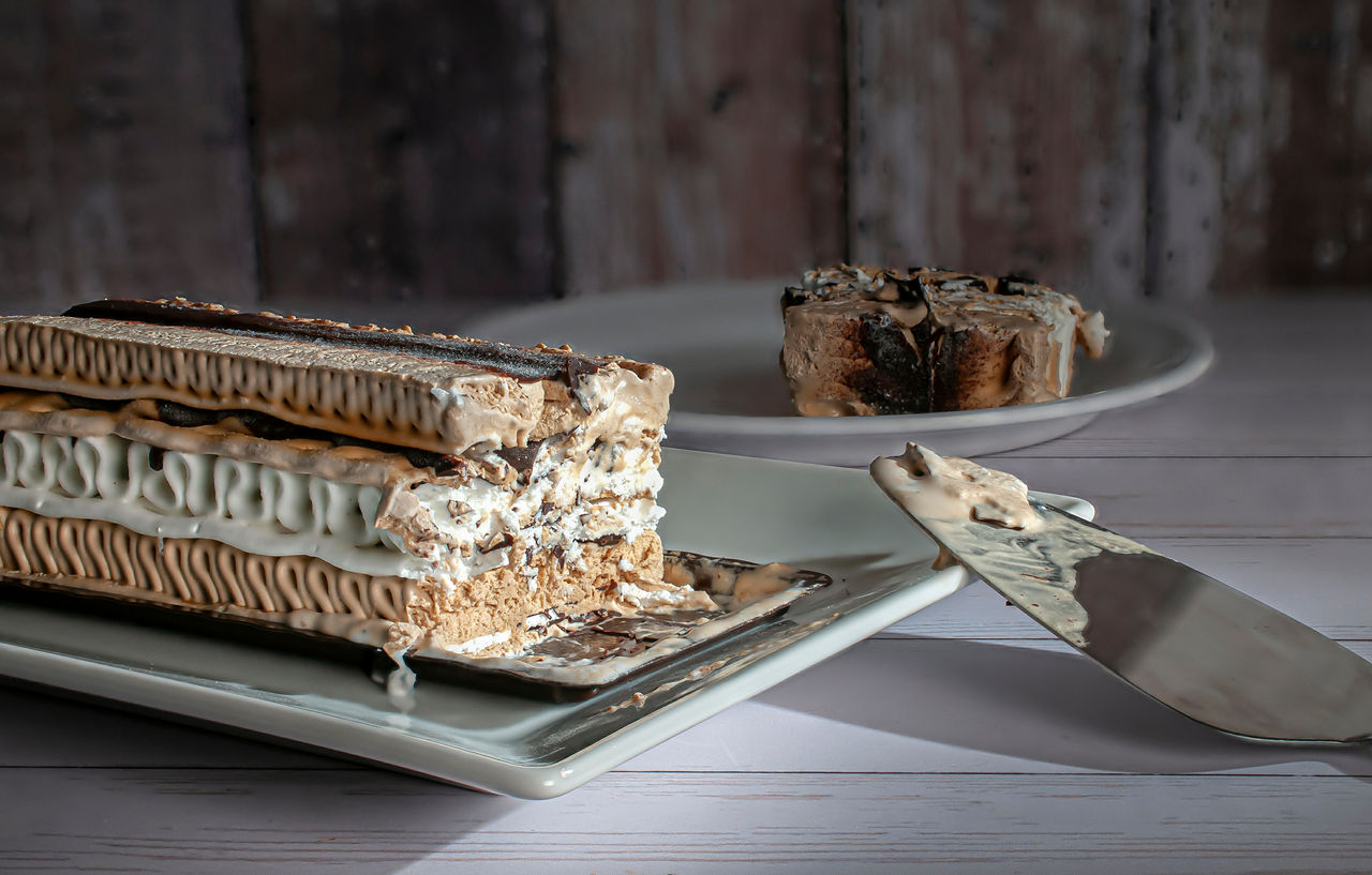 A rectangle shape coffee moka ice cream cake on a white plate with a slice served in the background