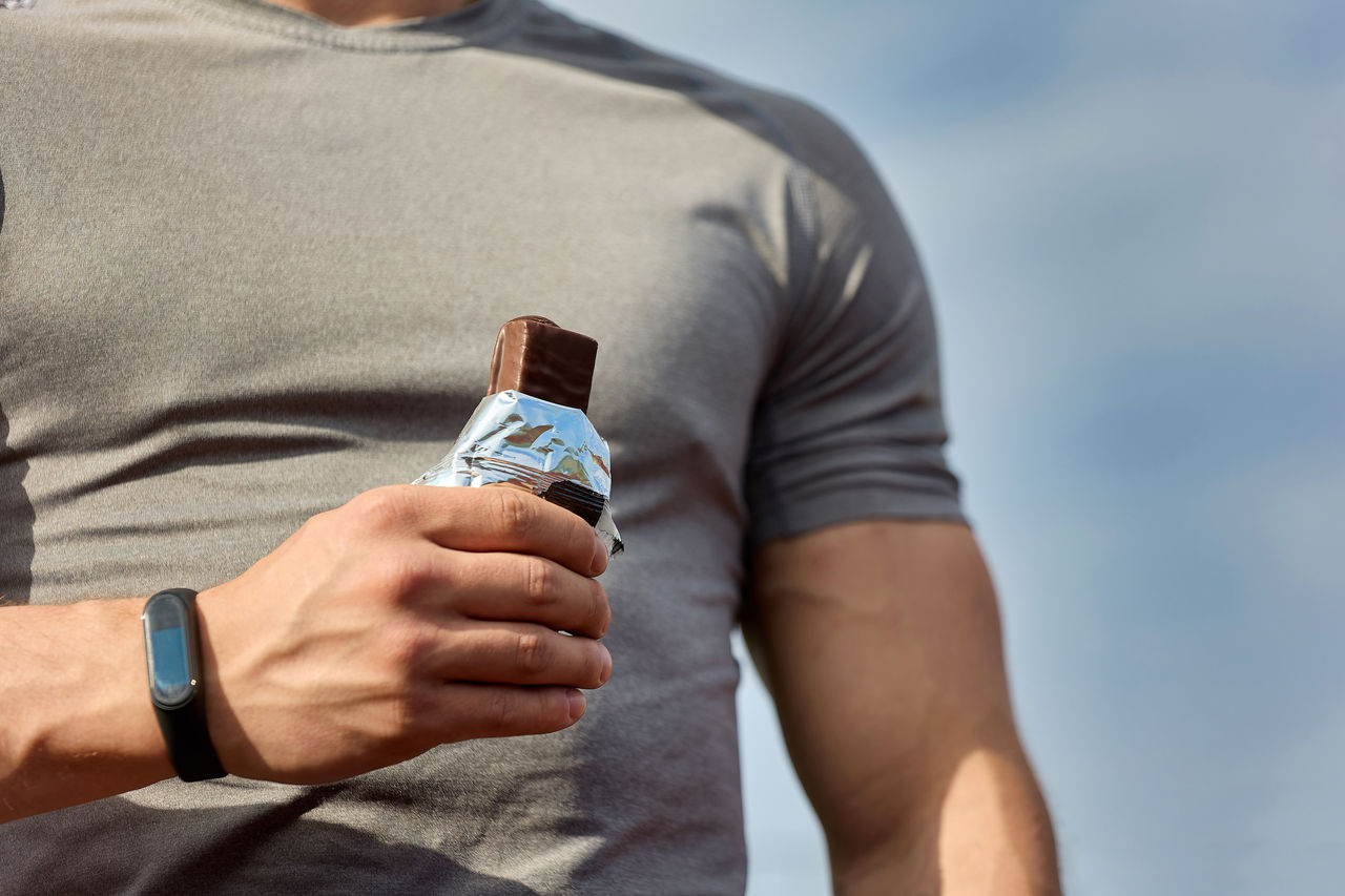 Muscular athlete rests after a workout, an athlete eats a protein bar. A young athlete eats an energy bar while enjoying chocolate after a hard workout at the stadium