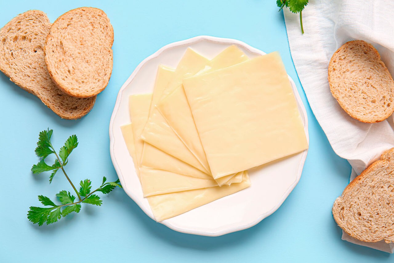Plate of tasty processed cheese with bread on blue background