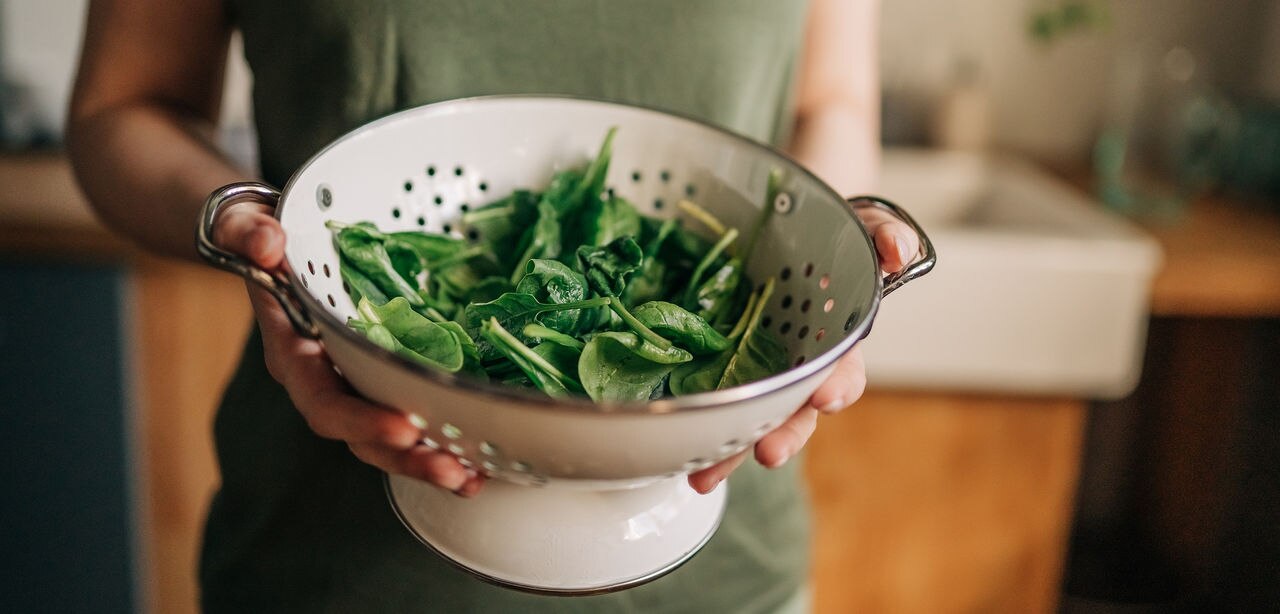 Green vegan breakfast meal in bowl with spinach, arugula, avocado, seeds and sprouts. Girl in leggins holding plate with hands visible, top view. Clean eating, dieting, vegan food concept
