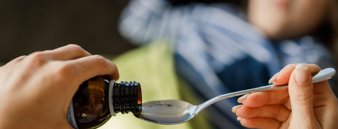 Close up of unrecognizable single mother pouring syrup into the spoon for her sick child.