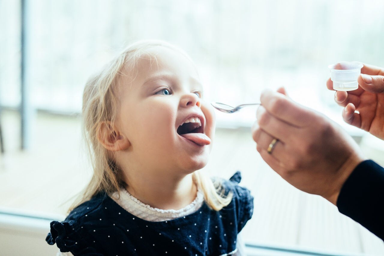 Mother giving medicine cough syrup to her little daughter at home.