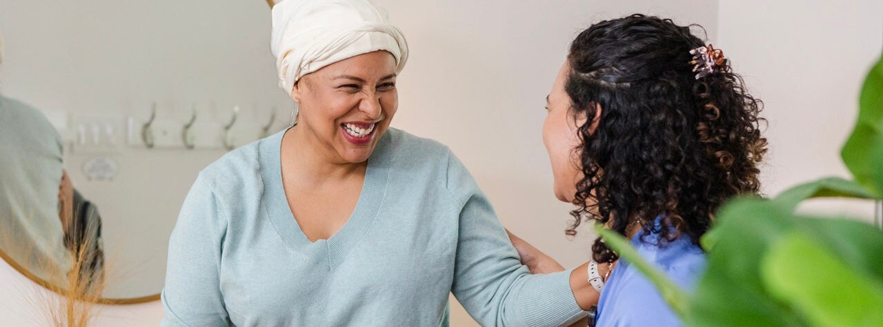 When the young adult female hospice nurse arrives, the mid adult female cancer patient greets her with a smile.