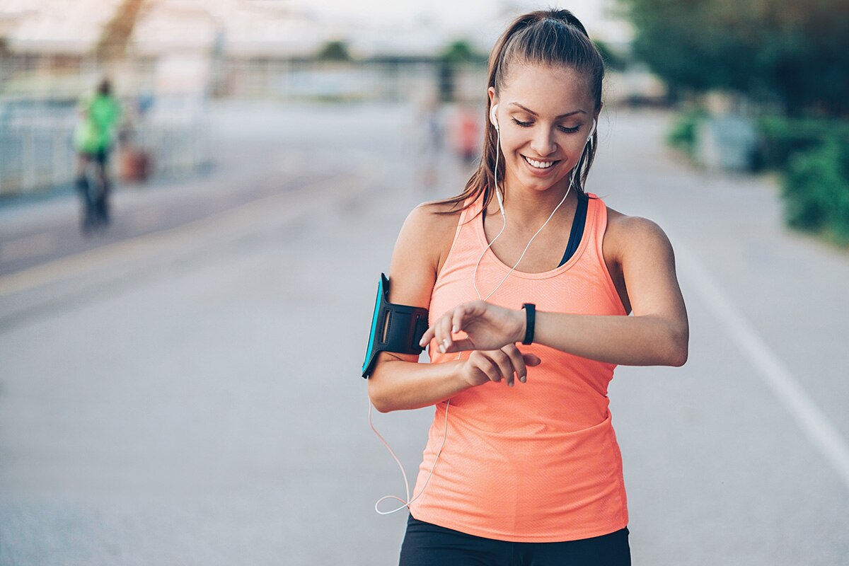 Smiling young sportswoman with arm band and headphones