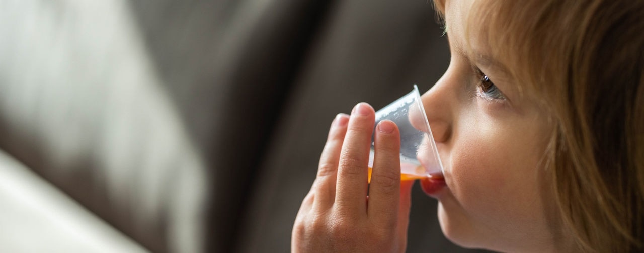 Cute little boy drinking cough syrup from a dose at home. Copy space.