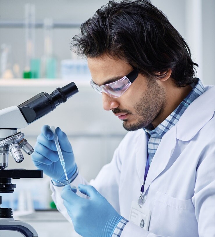 Young serious chemist in labcoat dropping liquid substance into petri dish while creating new compound during scientific experiment