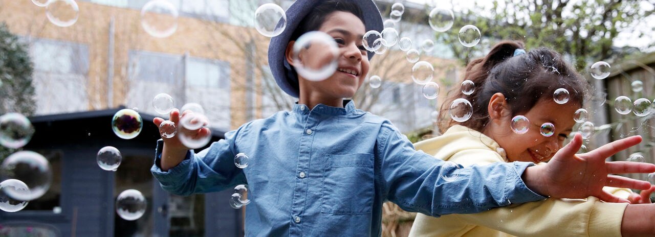 Brother and sister in garden surrounded by bubbles, carefree, playing, childhood