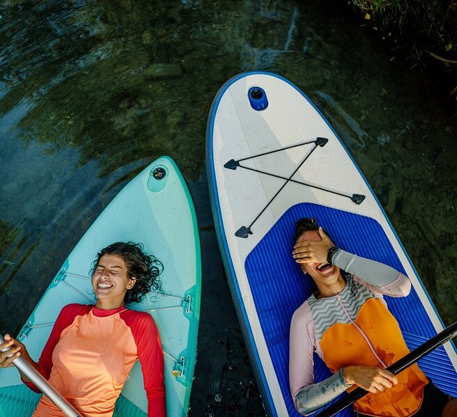 Photo of two teenage girls lying on their stand-up paddleboards and having a great time; teenagers hanging out in nature and enjoying their summer vacation.