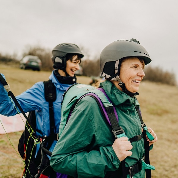 Photo of smiling senior woman and her instructor before the flight with a paraglider