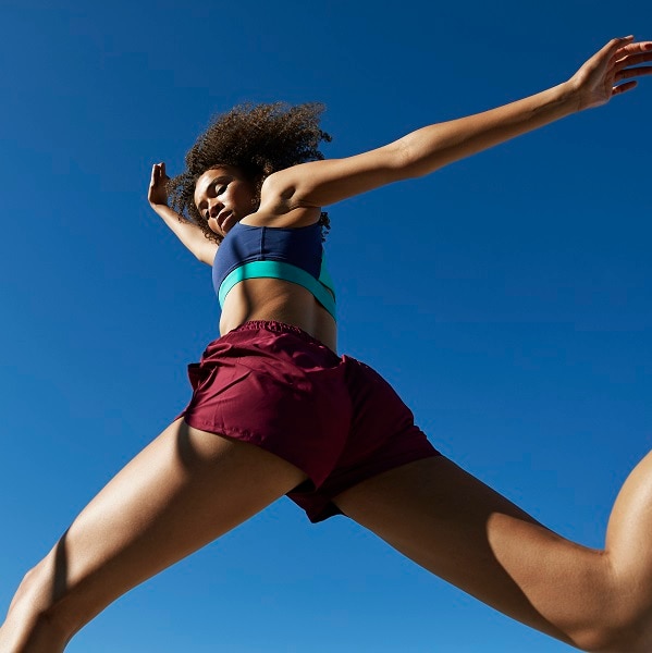 Frizzy young female athlete jumping against clear blue sky on sunny day