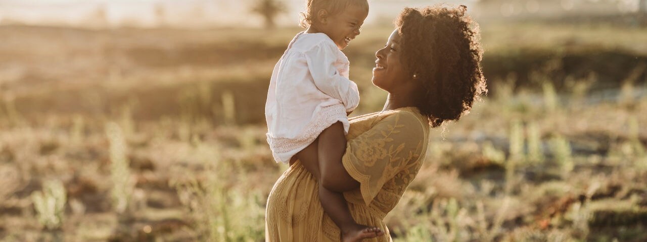 A pregnant African woman with her hands on her back smiling into the distance.