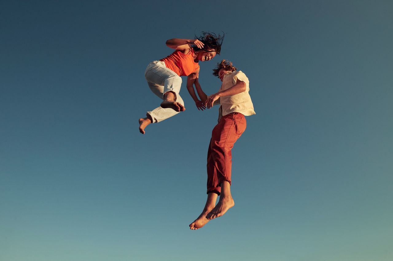 Low angle view of cheerful friends jumping high up in mid-air against clear blue sky