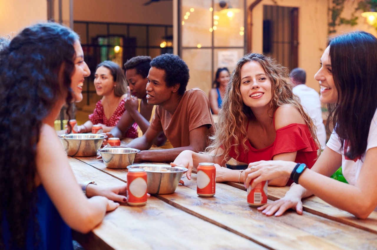 Smiling group of diverse young people talking together over beers while sitting outside on the patio of their hostel