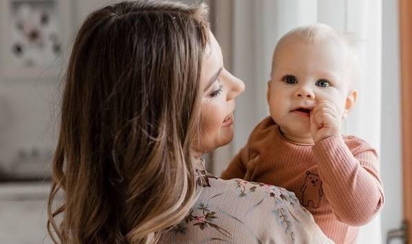 Young woman mom with baby girl on hands near window at home